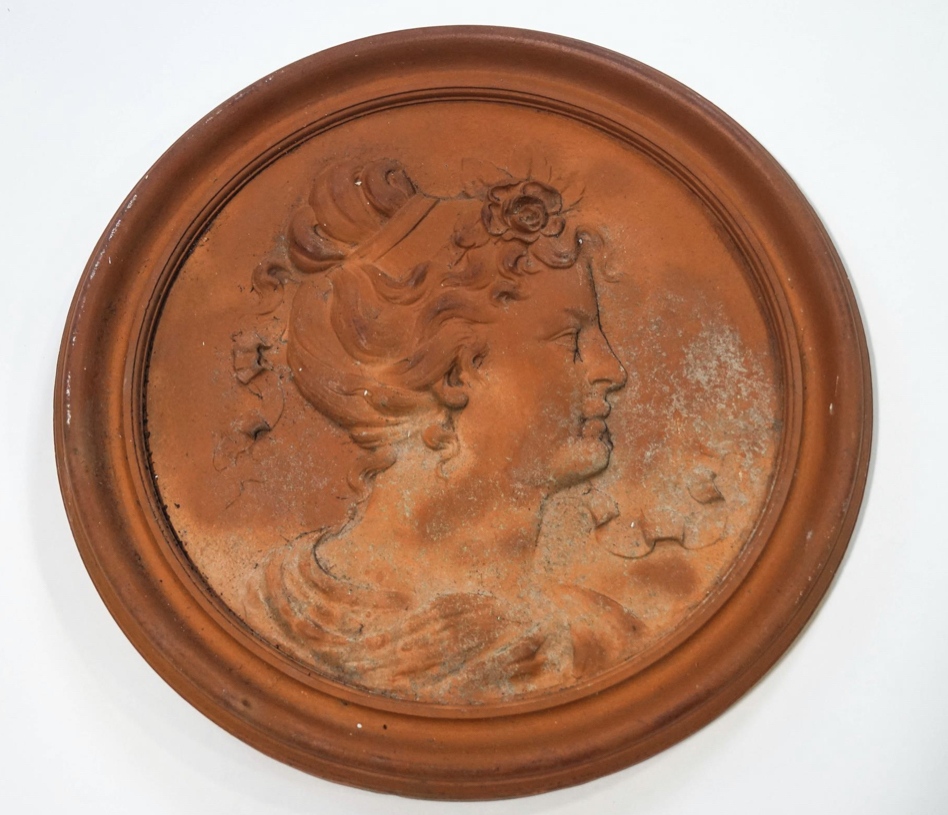 A terracotta roundel moulded with a ladies profile with ribbons in her hair,