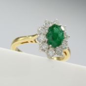 A 0.80ct oval-cut emerald and 0.50ct round brilliant-cut diamond cluster ring in 18ct yellow gold