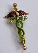 An 18ct gold enamel brooch in the style of the hypocratic oath with intertwined serpents, wings with