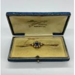 A Bar Gold Brooch with oval blue sapphire 6.5mm x 4.5mm, surrounded by 8 half seed pearls. Stamped