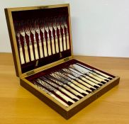 A cased set of ornate knives and forks in a wooden case.