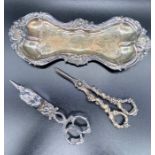 A candle snuffer and a pair of grape scissors and a tray.