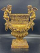 A gilt decorative modern urn with sitting angel cherubs to sides