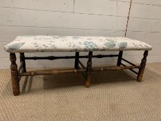 An upholstered low ottoman raised on turned legs (H35cm W94cm D35cm)