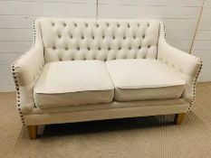 A two seater button back cream sofa with stud details to arms (H83cm W136cm D76cm)
