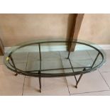 An oval glass coffee table on metal legs terminating on camel style feet L130 x H42 X W72cm