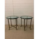 A pair of glass lamp tables on metal bases terminating on camel style feet (H62cm Dia62cm)