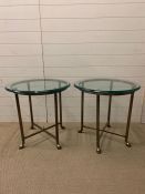 A pair of glass lamp tables on metal bases terminating on camel style feet (H62cm Dia62cm)