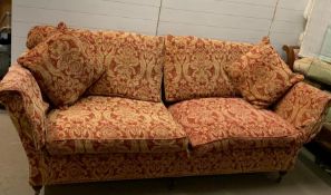A three seater sofa with floral red and gold coloured upholstery on brass castors (H86cm W230cm
