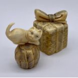 Two carved lidded netsukes, one a box with a bow and the other a cat on a ball of wool.
