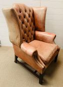 A George II style wing armchair with leather upholstered and deep button back over a loose cushion