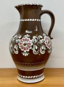 A substantial pottery pitcher or jug with floral decoration on brown grounds, 41 cm high by Gmundner