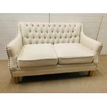 A two seater button back cream sofa with stud details to arms (H83cm W136cm D76cm)