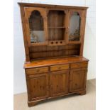 A pine dresser with glazed doors to top and cupboards to base (H190cm W133cm D45cm)