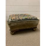 A tapestry footstool on brass bun feet