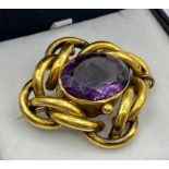 A Pinchbeck brooch with safety chain and central purple stone.