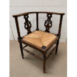 A mahogany corner chair with a straw seat and a carved harp design to back