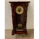 A mahogany wall clock with turned pillars to case and glazed door opening to reveal clock face (