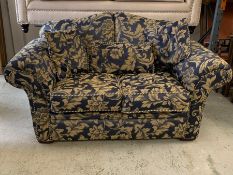 A two seater floral pattern sofa with scrolled arms and scatter cushions