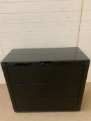 A black glass chest of drawers with faux shagreen chips to top and sides, working order (H88cm W90cm