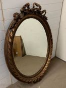 An oval gilt wall mirror with ribbon details to top and bottom (94cm x132cm)