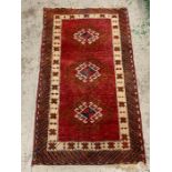 A small red grounds runner style rug with diamond shapes to centre (130cm x 76cm)