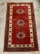 A small red grounds runner style rug with diamond shapes to centre (130cm x 76cm)