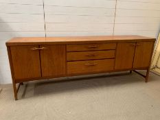 A Mid Century teak sideboard, drawers to centre and cupboards to ends (H79cm W214cm D45cm)