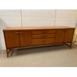 A Mid Century teak sideboard, drawers to centre and cupboards to ends (H79cm W214cm D45cm)