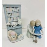 Two china ornaments, one of boy and girl sitting and reading and other of two cats and a bookcase