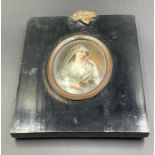 A framed small portrait on porcelain of a lay holding an oil lamp.