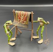 A cold painted bronze figure of two frogs beating a carpet.