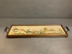 A needlework tray, needlework in cased under glass with brass and ebony handles on bun feet (W63cm)