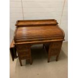 An oak roll top desk, opening to reveal drawers and pigeon holes (H110cm W113cm D72cm)