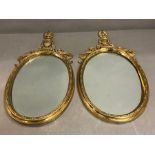 A pair of brass wall mirrors, oval shaped topped with trophy scrolling decoration