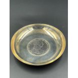 A white metal coin dish with a silver Austrian Maria Theresa Thaler to centre.