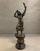 A metal sculpture of a lady waving from shore on pedestal base
