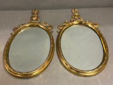 A pair of brass wall mirrors, oval shaped topped with trophy scrolling decoration