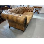 An oversized tanned leather chesterfield sofa, on castors, A/F