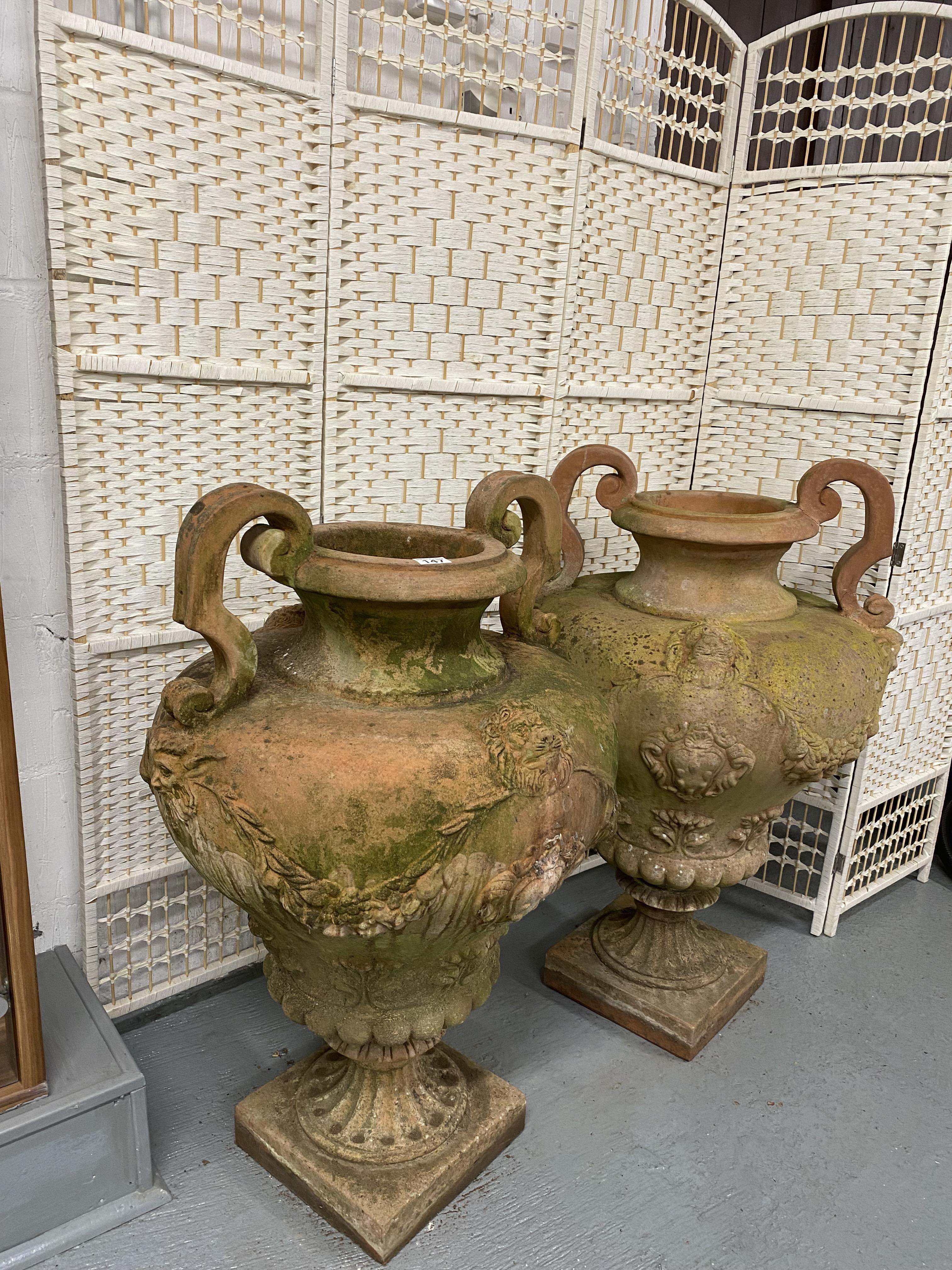 Two oversized Italian terracotta urns with twin handles, relief decorated with swags and lions.