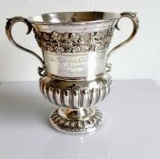 A George V two-handled silver trophy cup of waisted form with rococo and fluted decoration on a