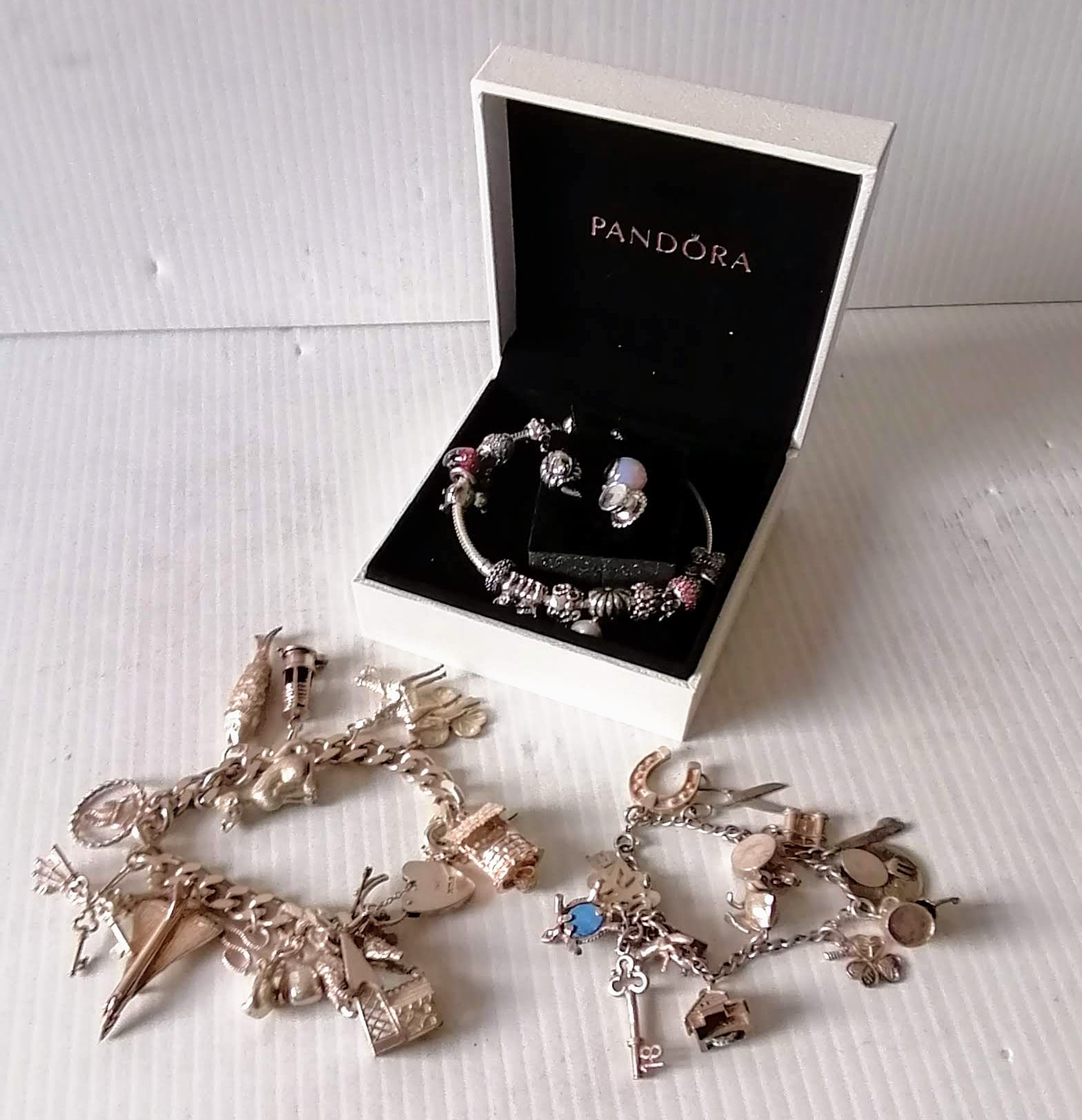 A Pandora charm bangle with original packaging and two other silver charm bracelets, 194g (3)