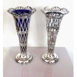 An Edwardian pair of pierced silver vases, one with blue glass liner, each on a stepped base by