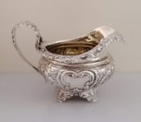 A George IV silver jug of squat form with profusely embossed floral and vine rococo design on four