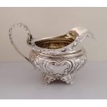 A George IV silver jug of squat form with profusely embossed floral and vine rococo design on four