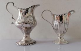 A George III silver creamer with serrated rim, scroll handle and floral design in relief on a raised