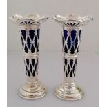 A pair of Edwardian pierced silver vases with trellis pattern, blue glass liners on stepped bases by