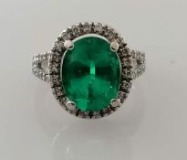 An oval emerald and diamond cluster ring, 10 x 7.9 5.35mm weighing a calculated 2.50 carats, vivid g