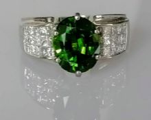 A tourmaline and diamond-set ring centrally set with an oval mixed-cut dark green tourmaline in a cl