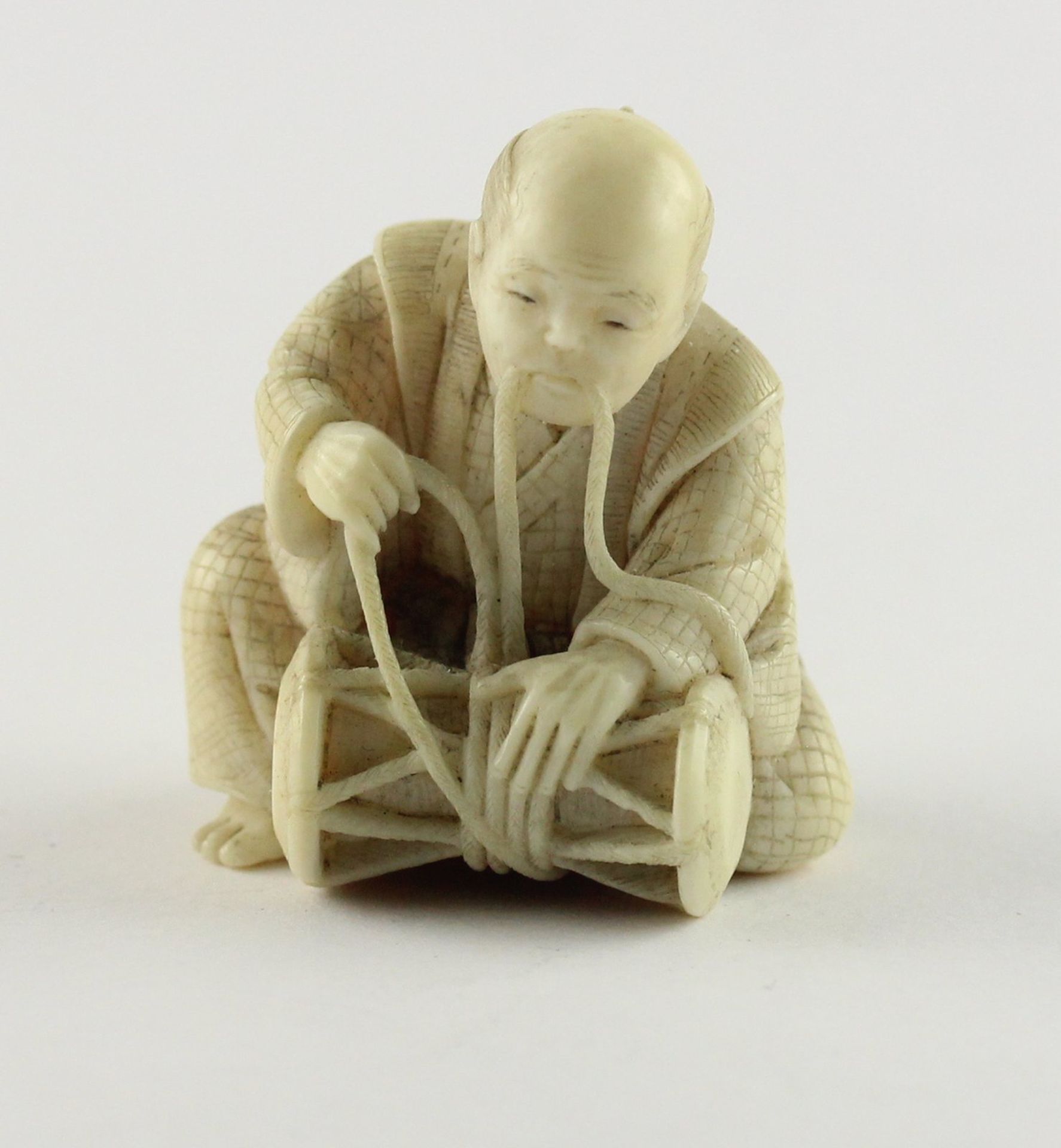 NETSUKE MANN BINDET EINE TROMMEL,